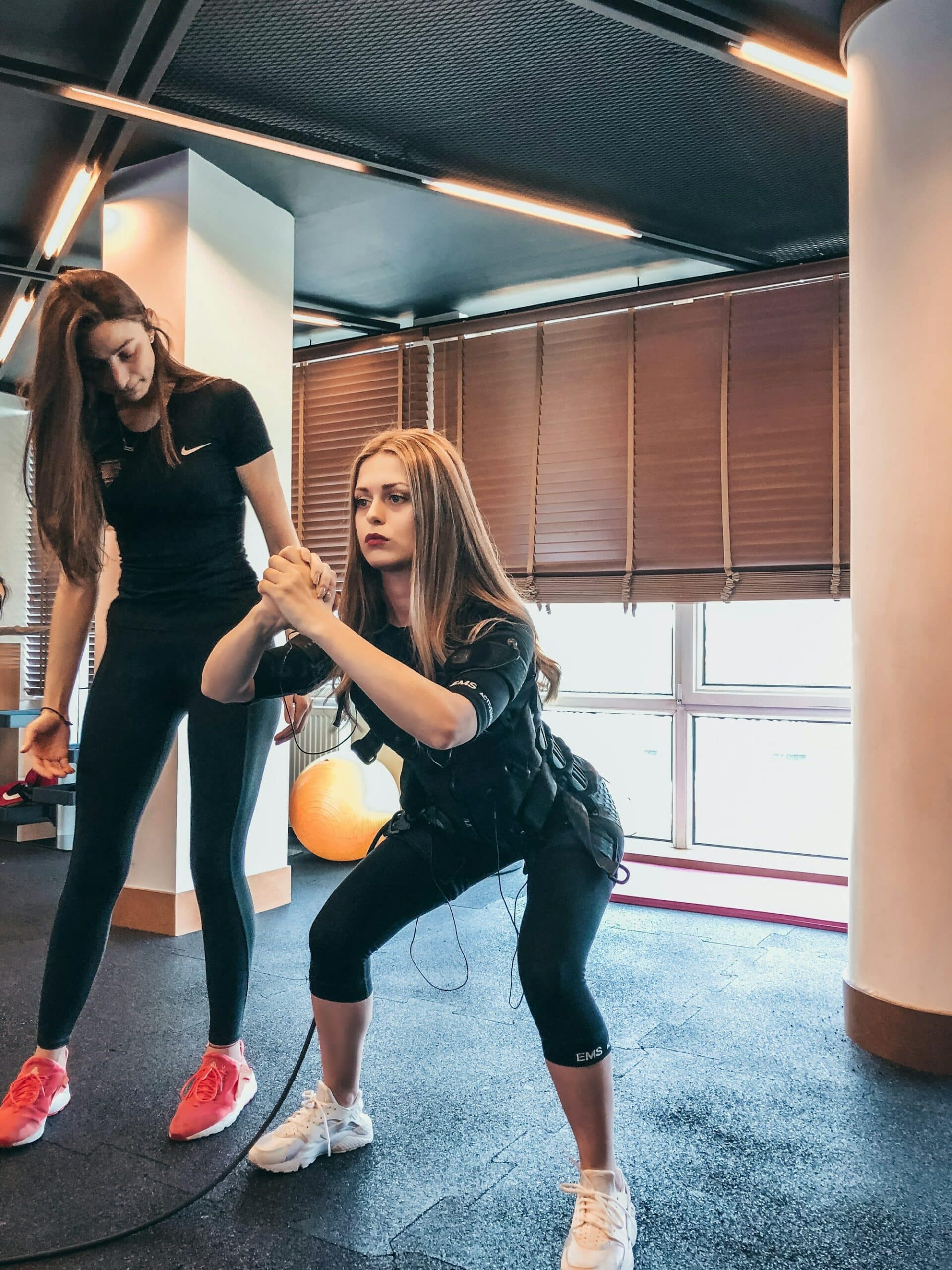 Coach sportive accompagnant une femme débutante sur un exercice de squat en salle de sport